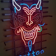 Neon sign of a devil creature with horns and a moustache, says "Tattoo" at the bottom