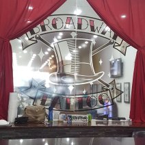 Frosted glass with "Broadway Tattoo" sign drawn across thhe centre and a drawing of a top hat. Framed by red curtains