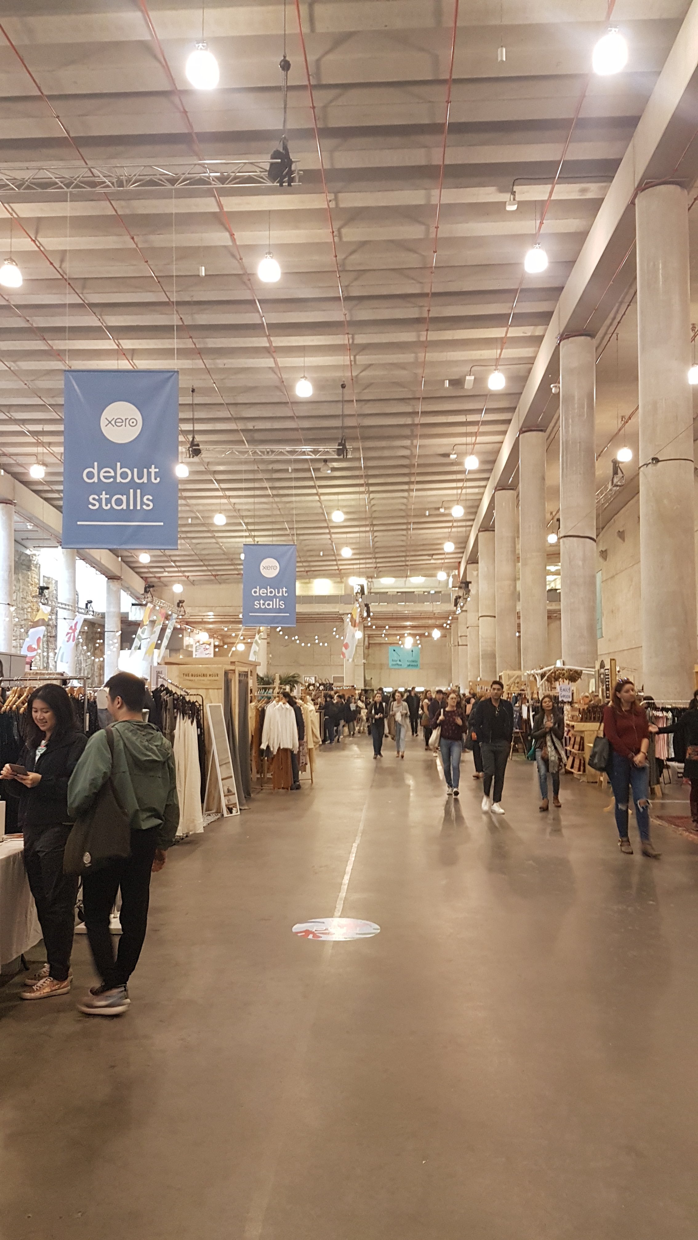 People stand in front of stalls in a large industrial space.